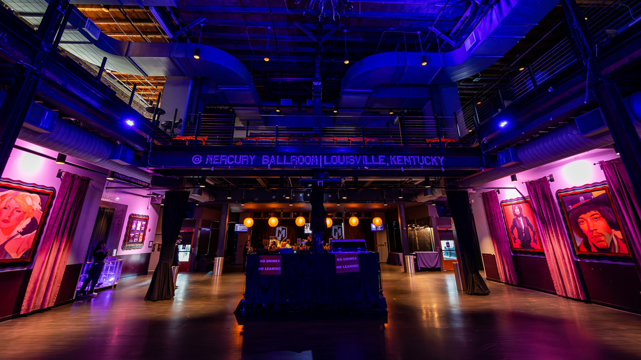 Mercury Ballroom interior with bold lighting, music portraits, a central bar, and an upstairs mezzanine.