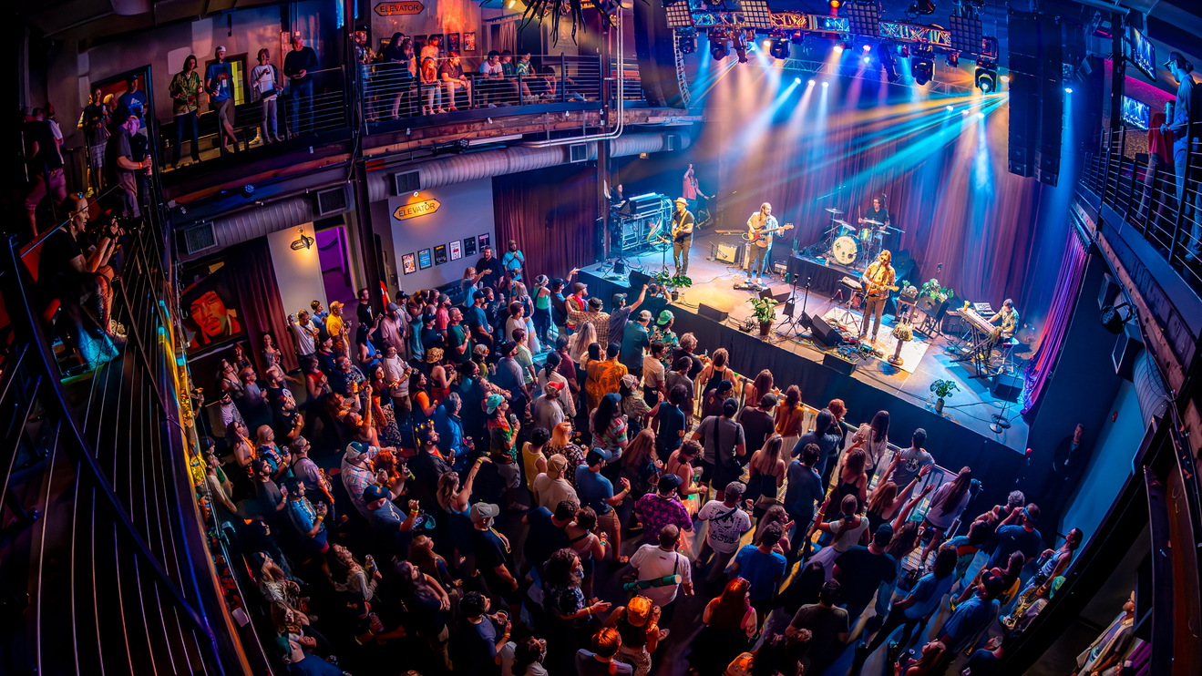 A packed crowd enjoys a live band under colorful lights at Mercury Ballroom