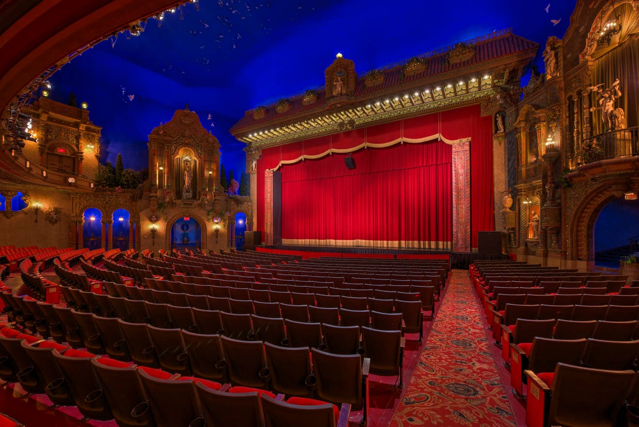 The ornate interior of the Louisville Palace, a historic theater with dramatic red curtains, intricate Spanish Baroque architecture, and a starry night sky ceiling.