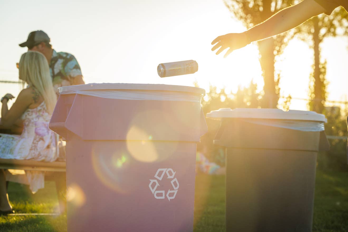 a hand throwing a can into the recycling bin