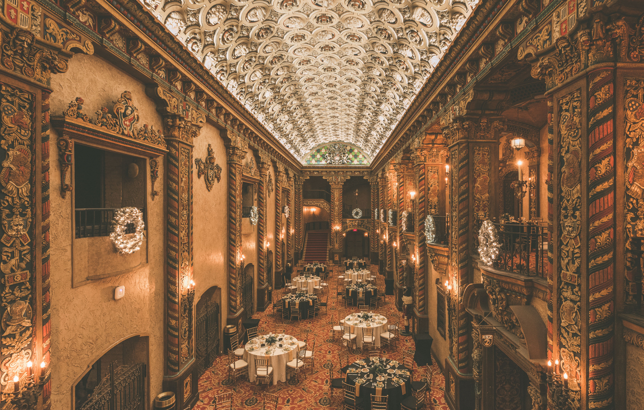 The ornate grand lobby of the Louisville Palace set up for a special event, featuring elegant round tables, golden chairs, warm lighting, and intricate architectural details under a stunning decorative ceiling.